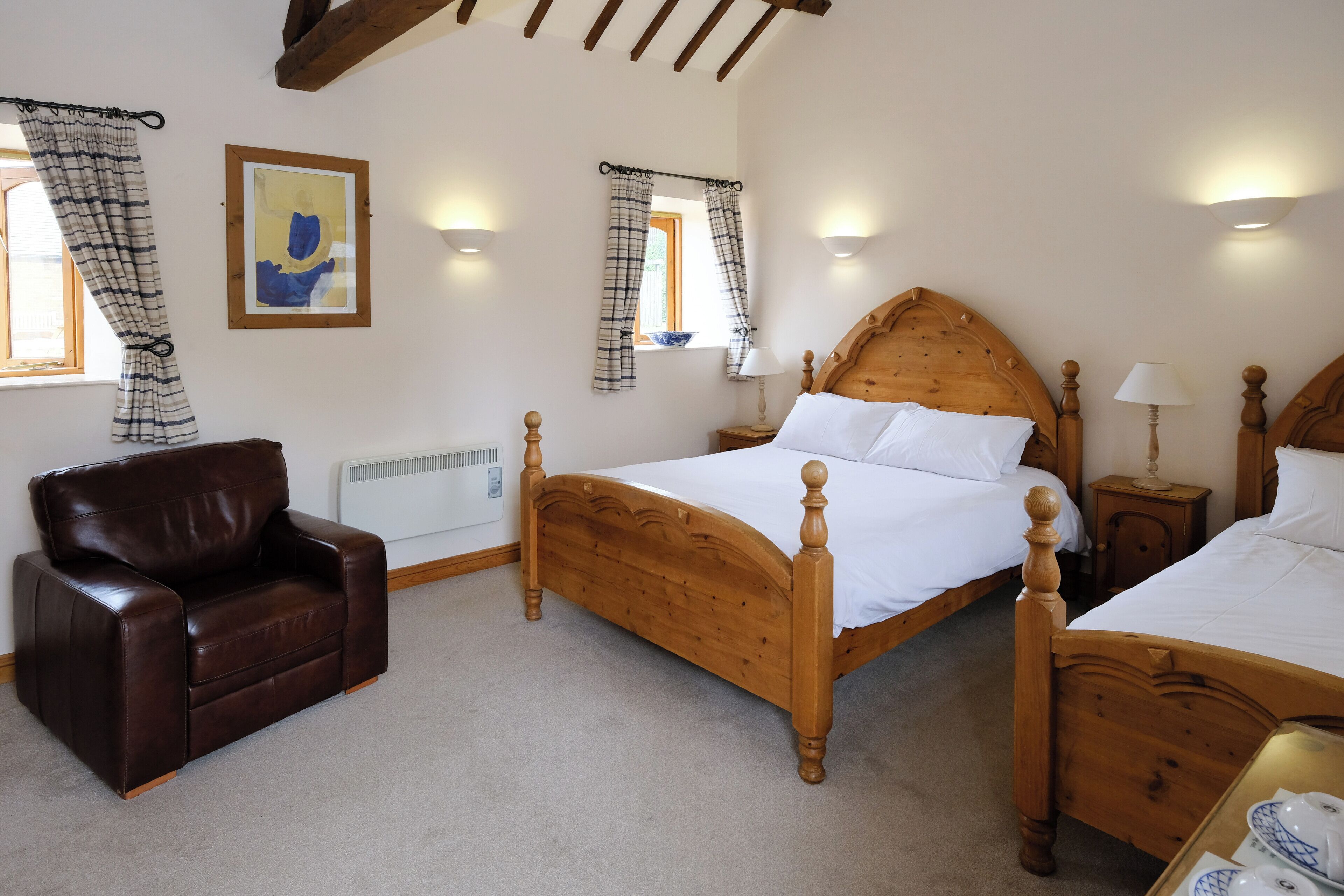 A bedroom with a wooden bed, a leather chair, and a framed picture on the wall.