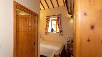 A wooden door leading to a bedroom with a bed, a window with curtains, and a desk with a telephone.