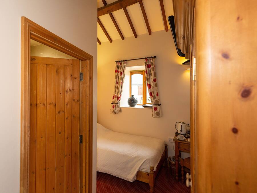 A wooden door leading to a bedroom with a bed, a window with curtains, and a desk with a telephone.