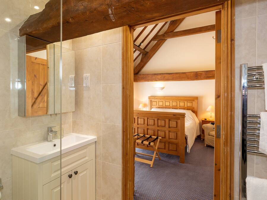 Una habitación de hotel con techo de madera, una cama grande, una mesita de noche y un baño con lavamanos y espejo.