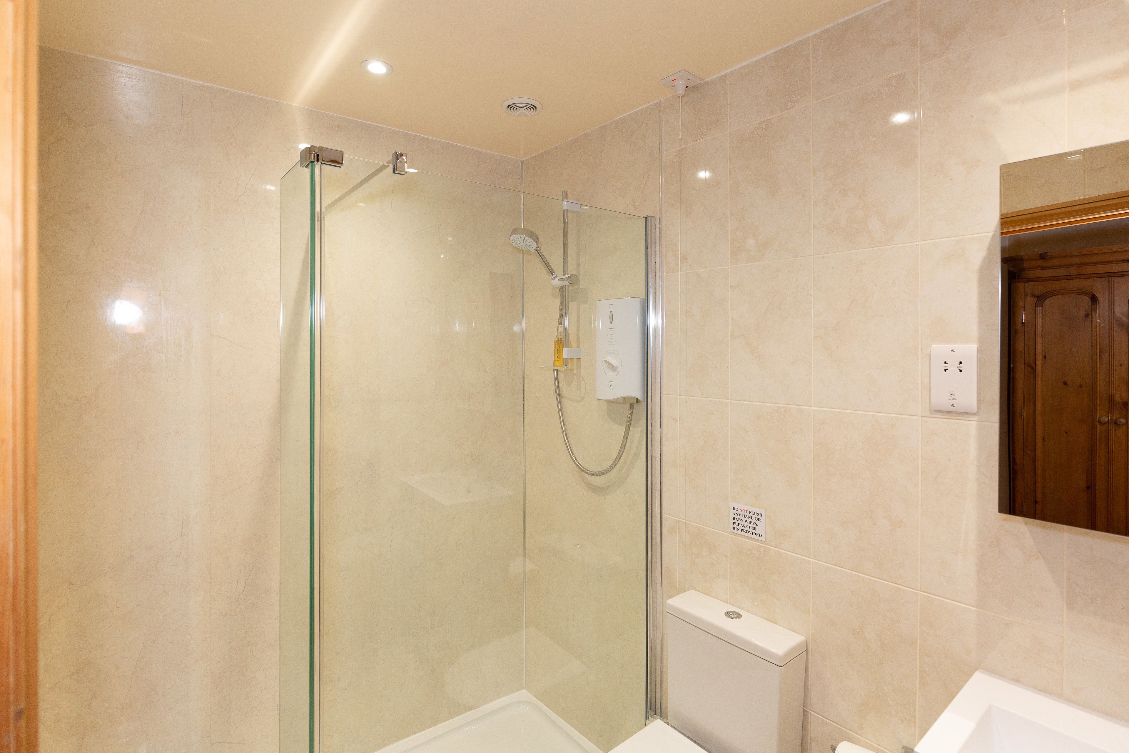 A modern bathroom with a glass-enclosed shower, a white bathtub, and a wooden cabinet.