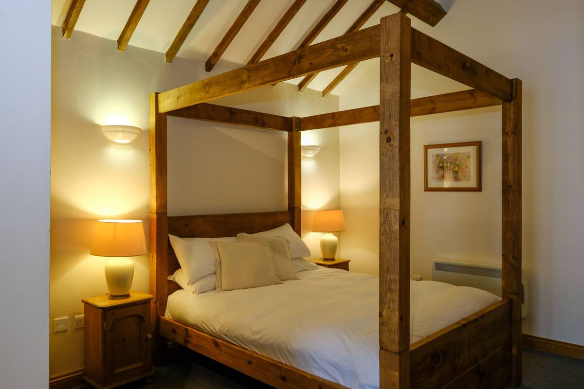 A four-poster bed with wooden beams, two bedside lamps, and a framed picture on the wall.