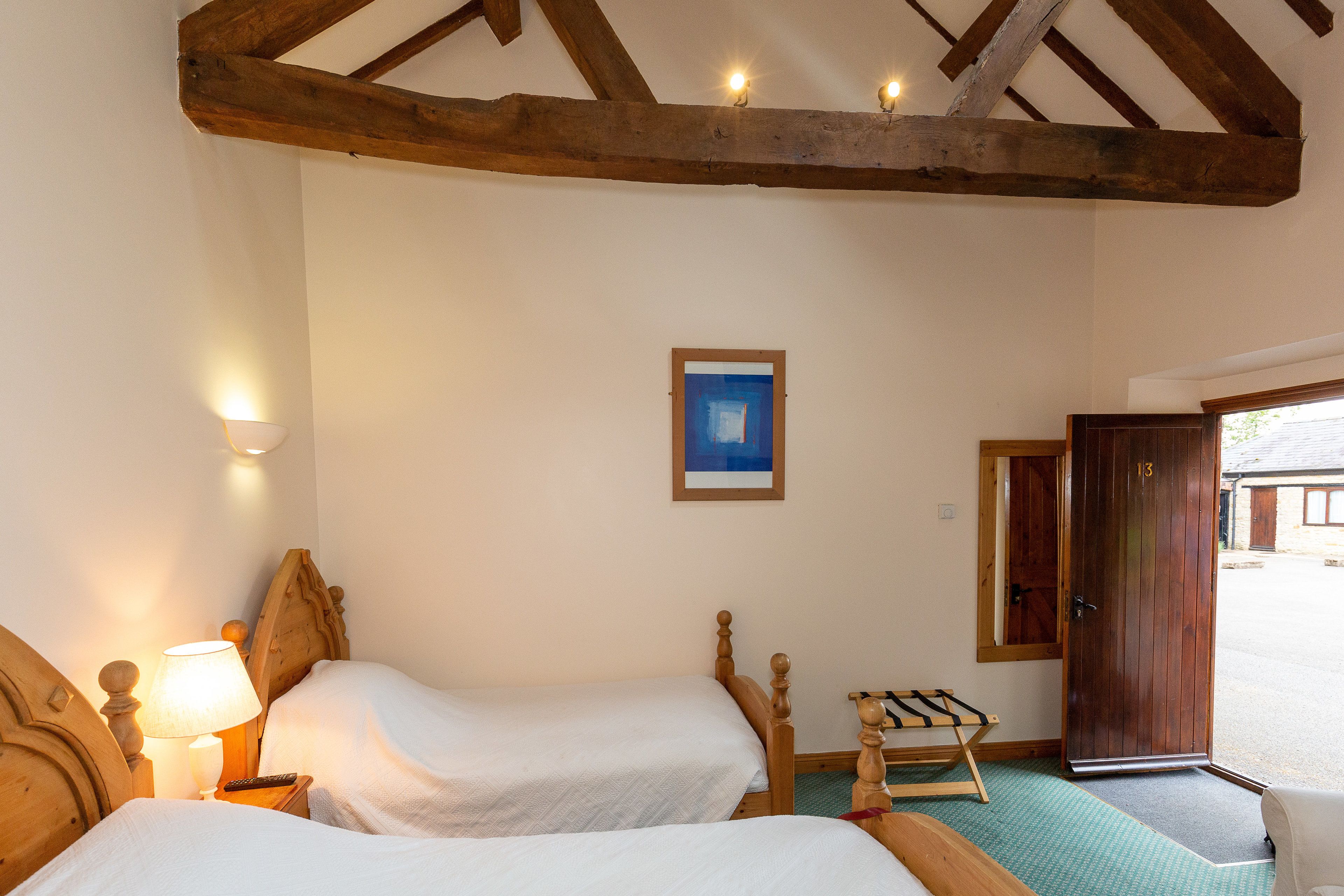 A room with two wooden beds, a nightstand with a lamp, a framed picture on the wall, and a door leading outside.