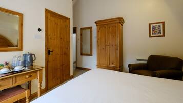 Quarto com cama, guarda-roupa de madeira, secretária com chaleira e poltrona marrom.