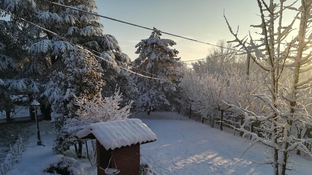 A snow-covered garden with a brick structure, possibly a gazebo, surrounded by snow-laden trees and a fence. - Villa Laura (Incisa Scapaccino)