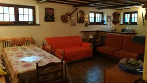 A cozy living room with a dining table, two sofas, a fireplace, and various wall decorations including a guitar and framed pictures. - Villa Laura (Incisa Scapaccino)