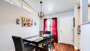 A dining area with a wooden table, chairs, and a chandelier. There are red curtains and a door in the background. - ★ Easy Check-in ★ By Downtown Littleton ★ Full Kitchen ★ (Littleton)
