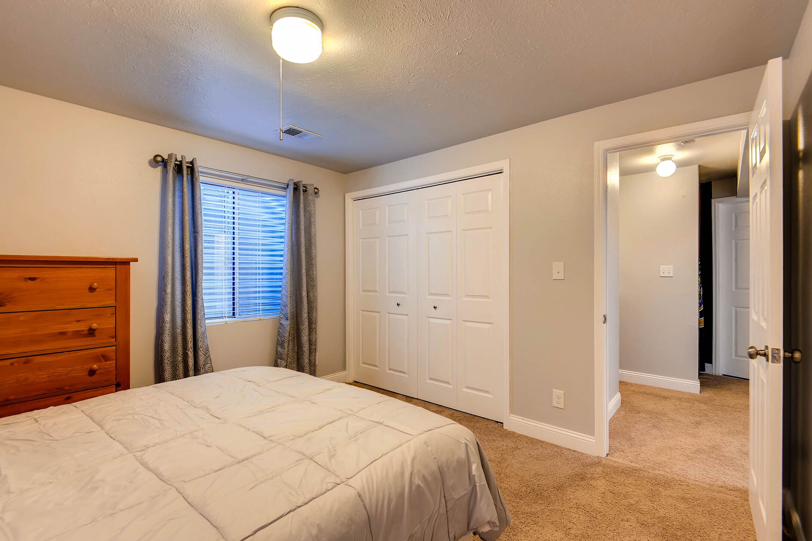 A bedroom with a bed, a dresser, a closet, and a door leading to another room.
