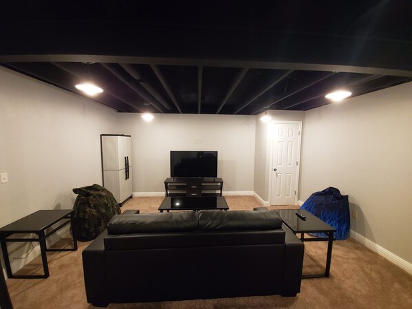 A living room with a black leather couch, a flat-screen TV, a white refrigerator, and a door.