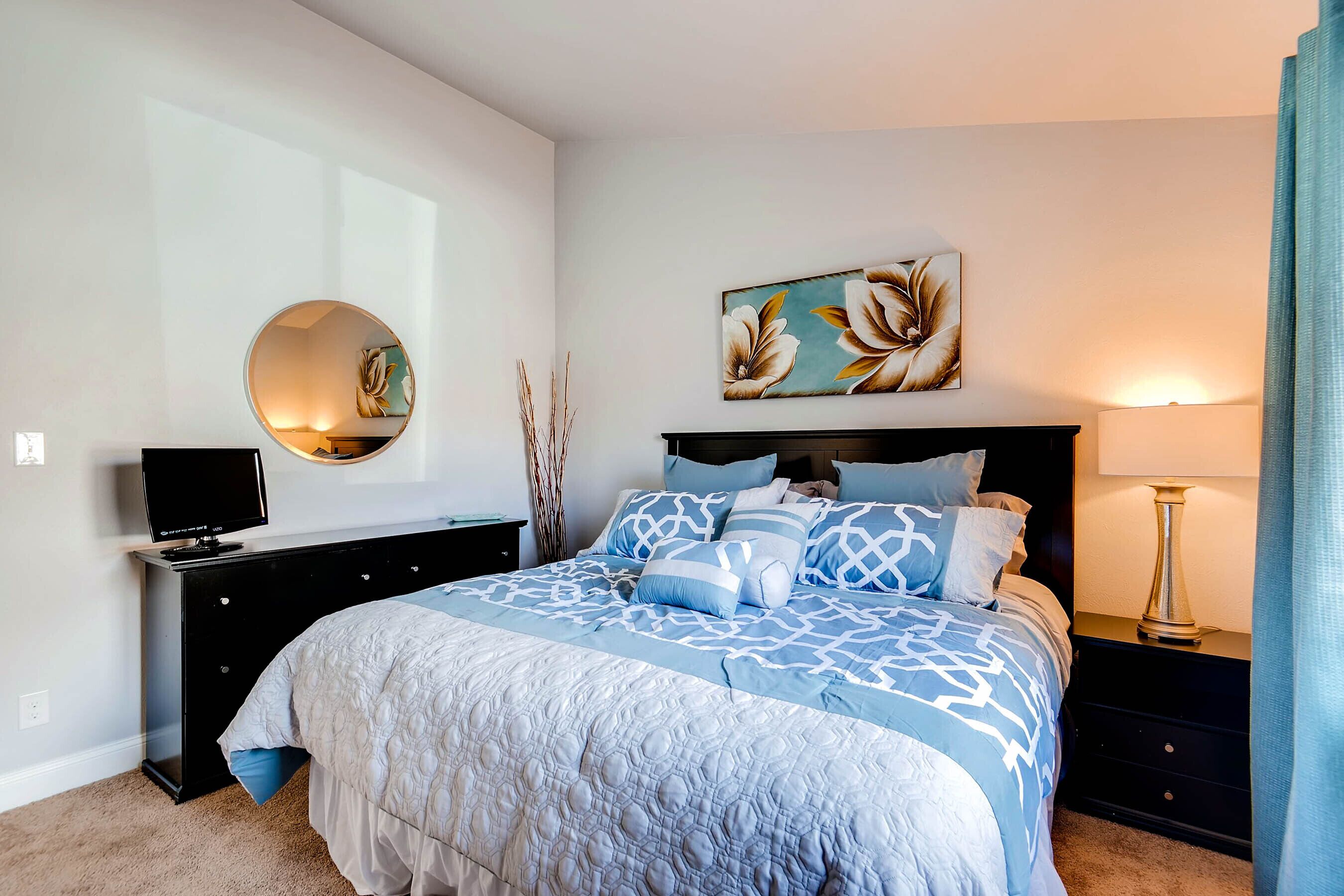 Une chambre à coucher avec un lit, une télévision, un miroir, un tableau et une lampe.