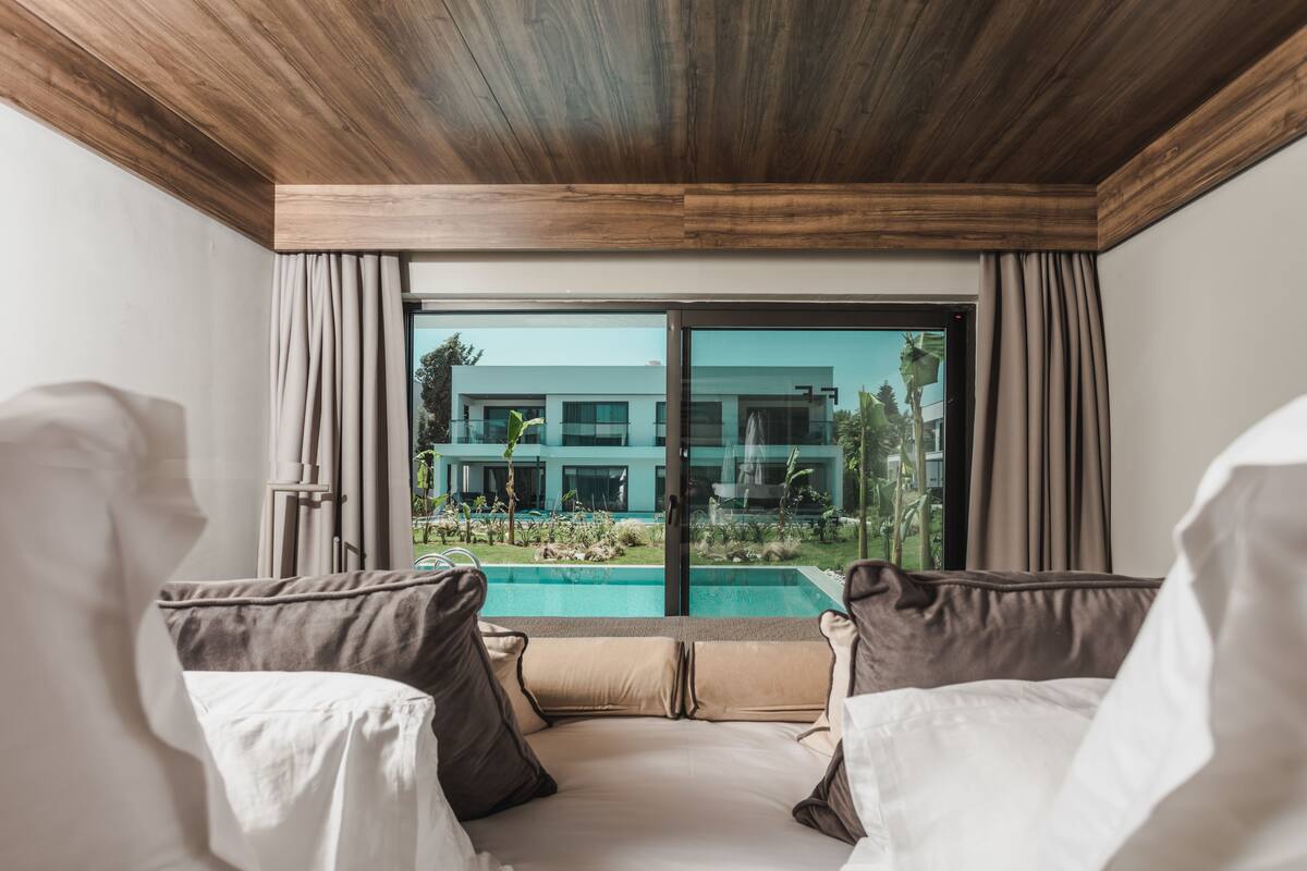 A bedroom with a large window overlooking a swimming pool and a modern building.