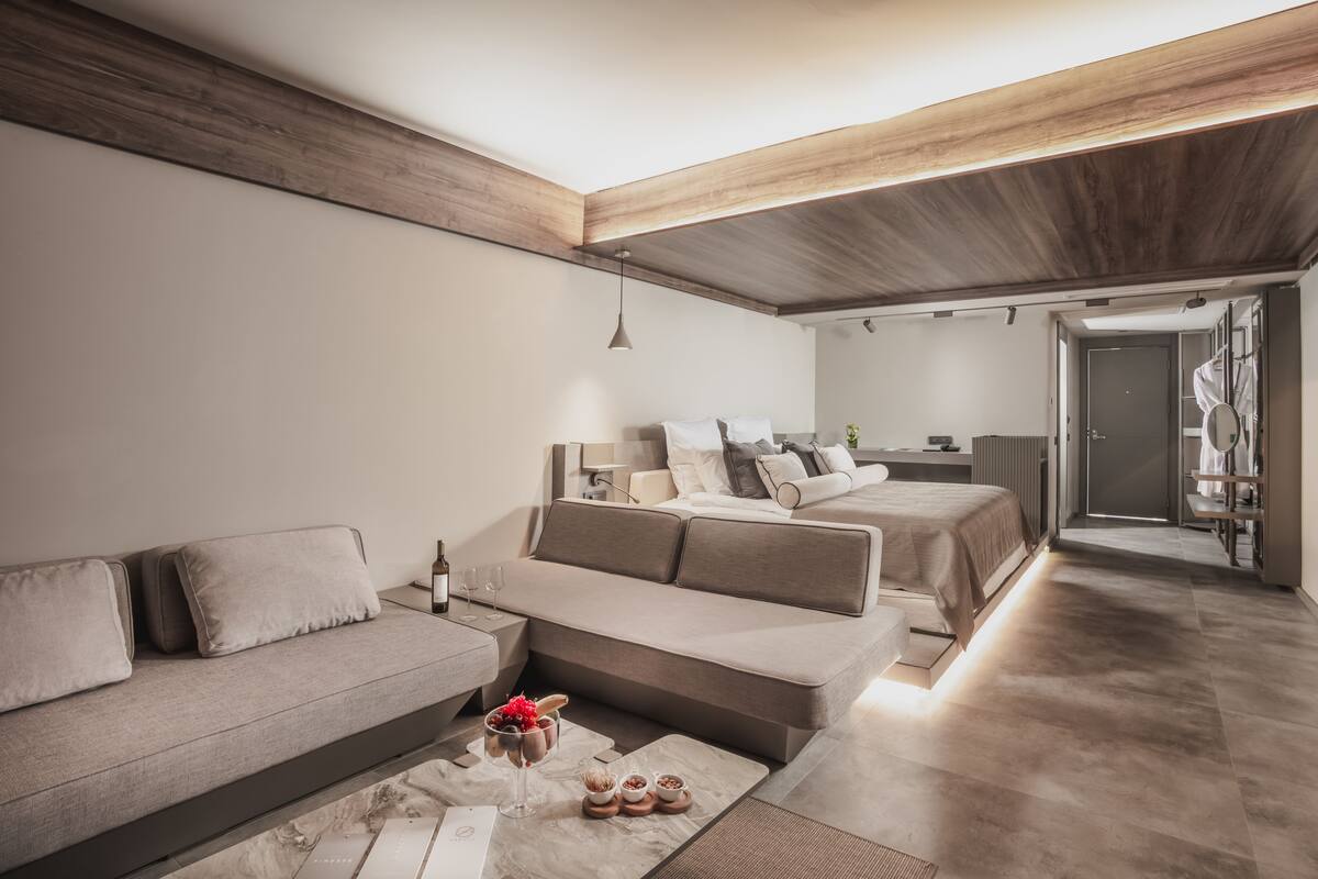A modern, minimalist bedroom with a sofa, a bed, and a small table with a drink and snacks.