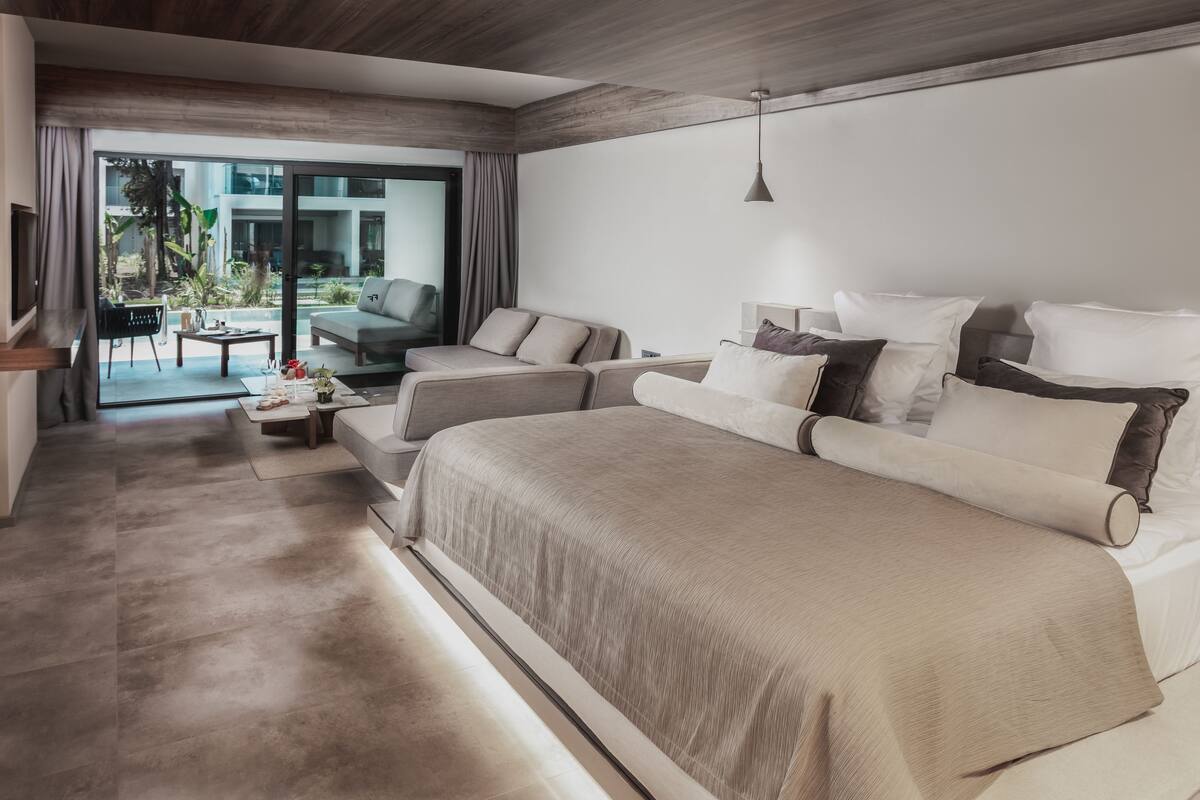 A modern hotel room with a large bed, a sofa, a coffee table, and a TV.