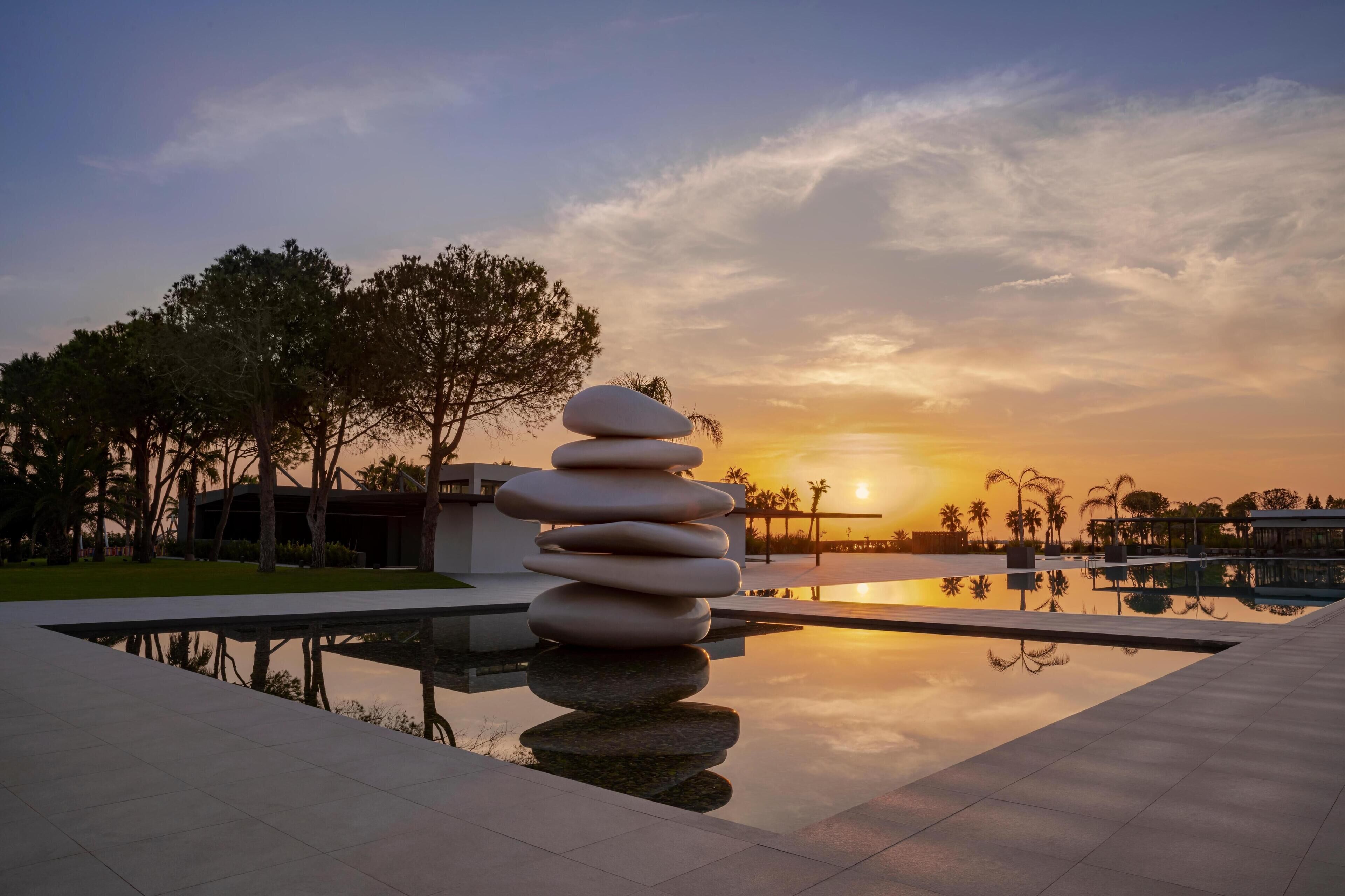 A serene outdoor setting with a stone stack, a reflective pool, and a sunset in the background.