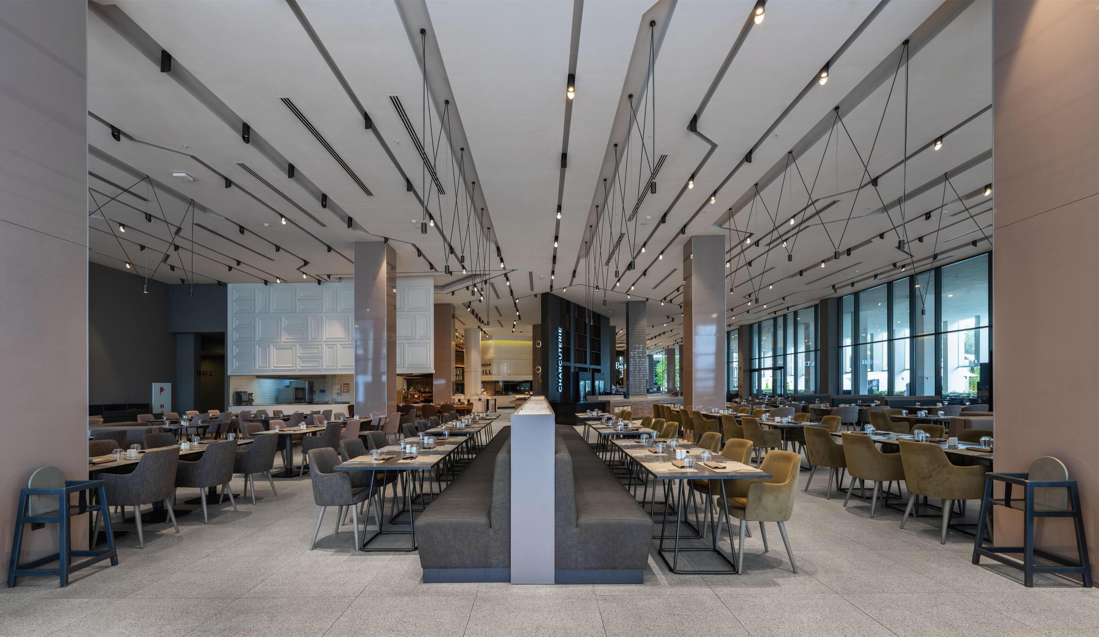 Un vaste espace dédié à la salle à manger, avec de nombreuses tables et chaises, de grandes fenêtres et une colonne centrale.