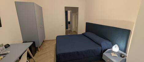 A bedroom with a bed, a desk, a chair, a wardrobe, and a nightstand.