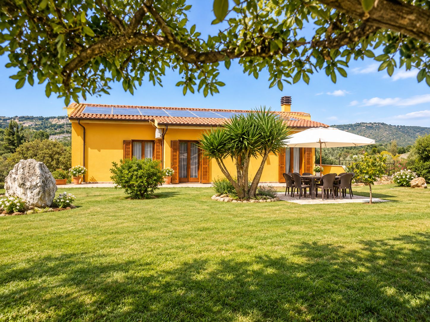 Eine gelbe Villa mit Ziegeldach, einer Terrasse mit Tisch und Stühlen und Blick auf die umliegende Landschaft.