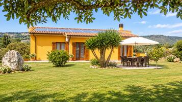 Eine gelbe Villa mit Ziegeldach, einer Terrasse mit Tisch und Stühlen und Blick auf die umliegende Landschaft.