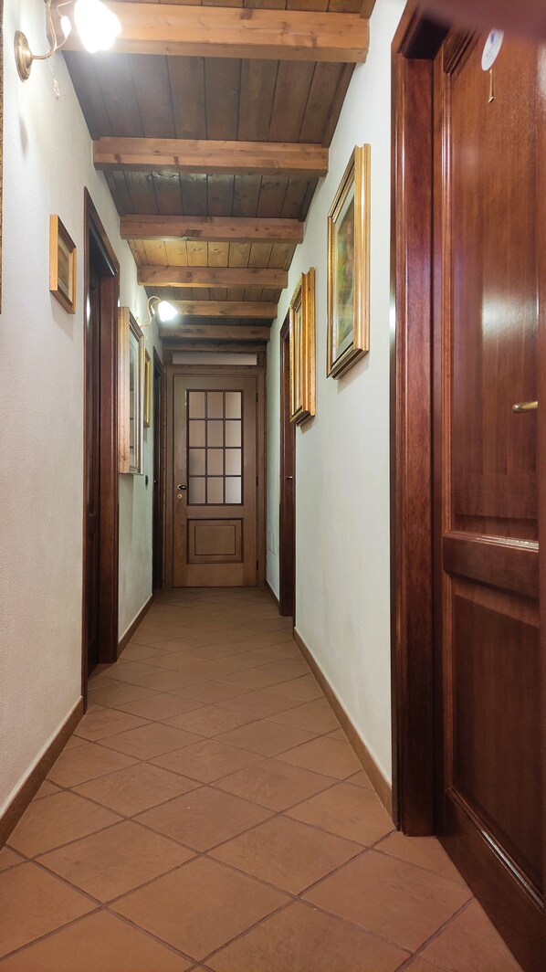 A hallway with wooden beams, tiled floor, and framed pictures on the walls. - La Grotta Delle Fate (Ossi)
