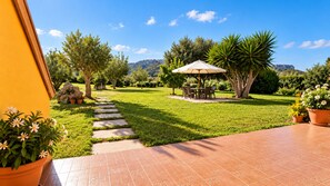 A garden with a paved walkway, a dining area with outdoor furniture, and a view of the surrounding landscape. - La Grotta Delle Fate (Ossi)