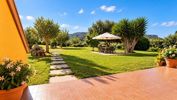 Un jardín con un camino empedrado, una zona de comedor con mobiliario exterior y vistas del paisaje circundante.