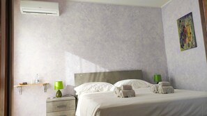 A hotel room with a bed, a nightstand, a green lamp, a painting on the wall, and an air conditioner. - La Grotta Delle Fate (Ossi)