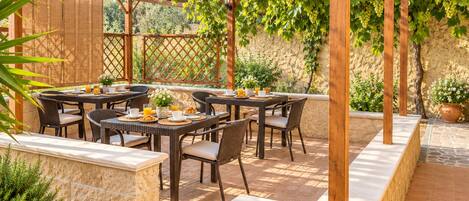 An outdoor patio with wooden pergola, stone walls, and a table set for breakfast.