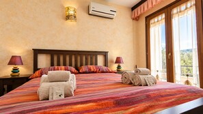 A hotel room with a large bed, two bedside lamps, an air conditioning unit, and a window with curtains. - La Grotta Delle Fate (Ossi)
