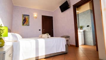 Ein Hotelzimmer mit einem Bett, einem Nachttisch, einer Lampe, einem Gemälde, einer Tür und einem durch eine offene Tür einsehbarer Badezimmer.