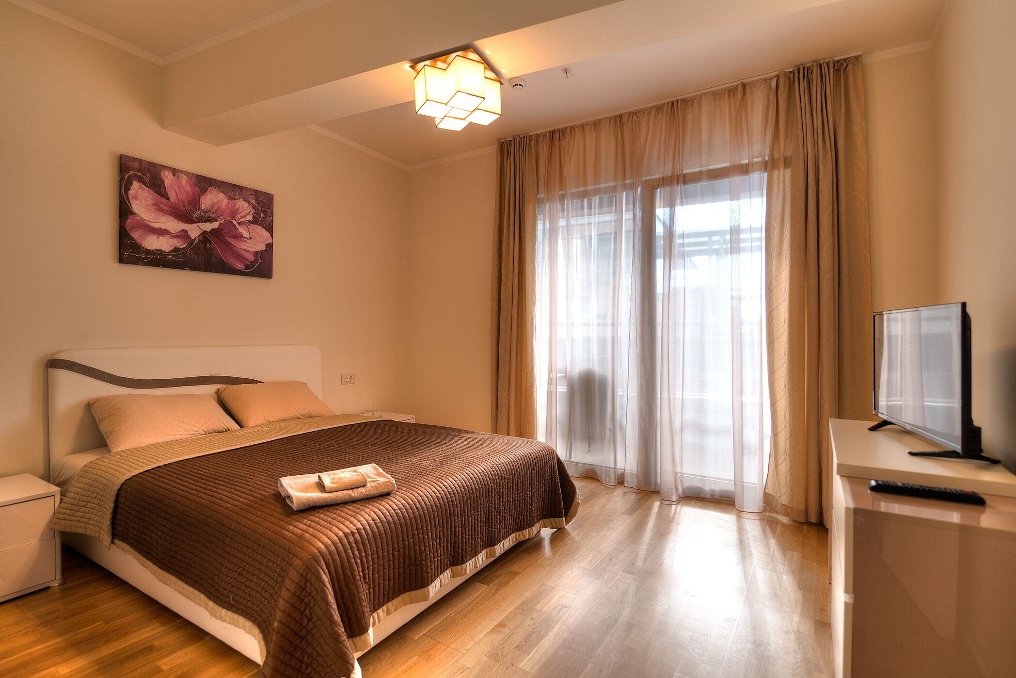 A neatly arranged hotel room with a large bed, a flat-screen TV, and a painting on the wall.