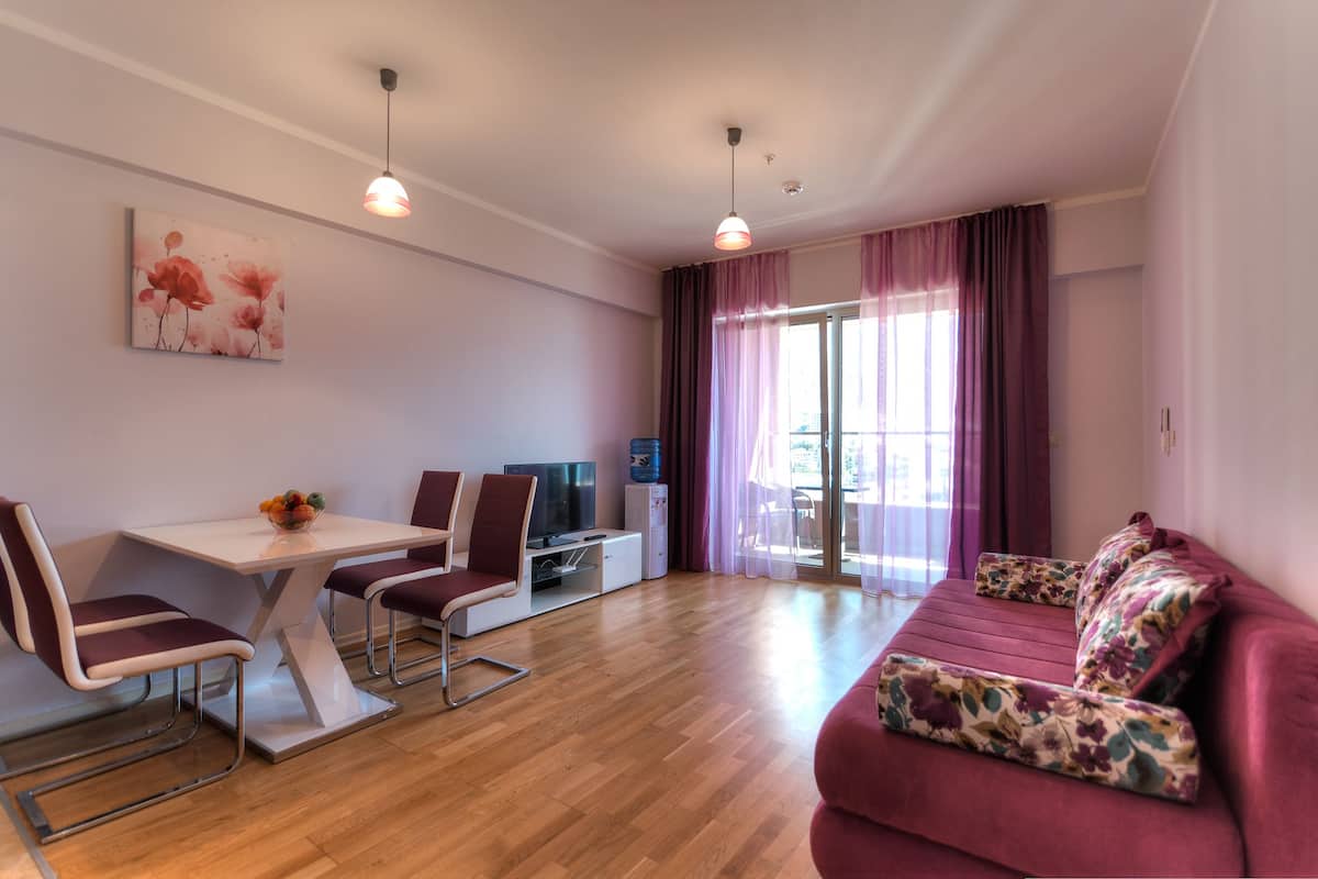 Una sala de estar moderna con un sofá, una mesa de comedor con sillas, un televisor y un amplio ventanal con cortinas.