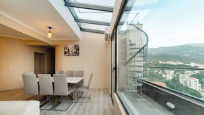 A modern apartment with a dining area, a balcony with a glass railing, and a city view. - Harmonia Colours (Budva)