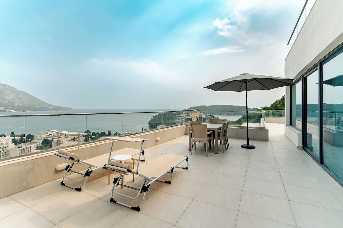 Una terraza en la azotea con vista al mar, una mesa con sillas y un toldo.