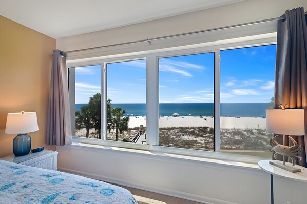 A hotel room with a large window offering a beach view, a bed with a blue and white patterned bedspread, and two lamps on side tables.