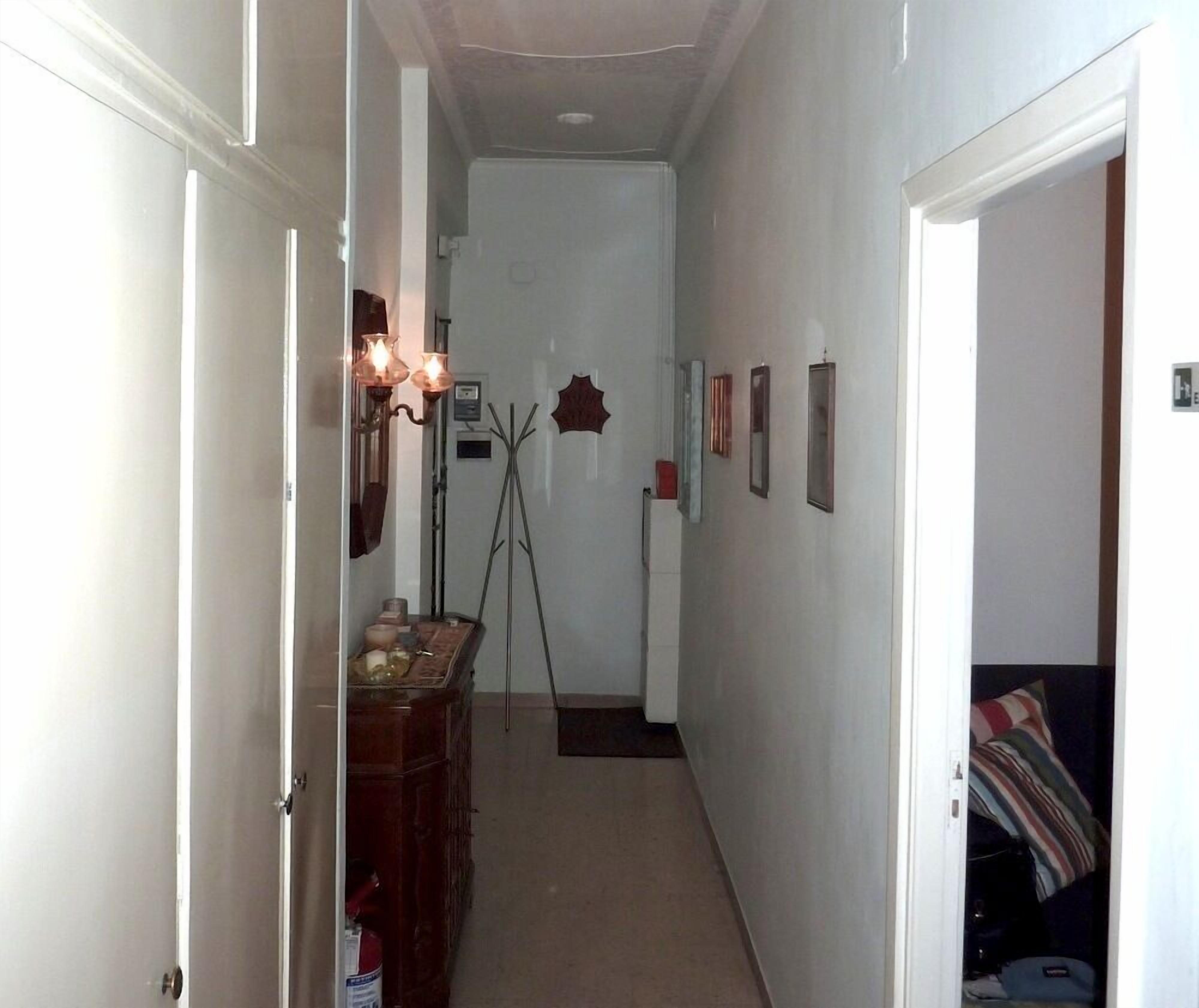 Un couloir étroit avec un porte-manteau, une petite table sur laquelle sont posés quelques objets, et une porte qui donne sur une pièce.