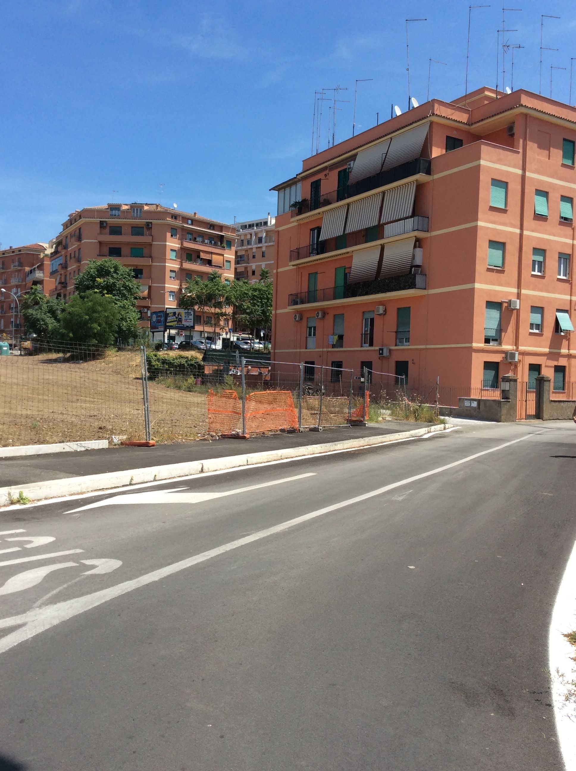 A multi-story residential building with balconies, a clear sky, and a road with a bicycle lane.