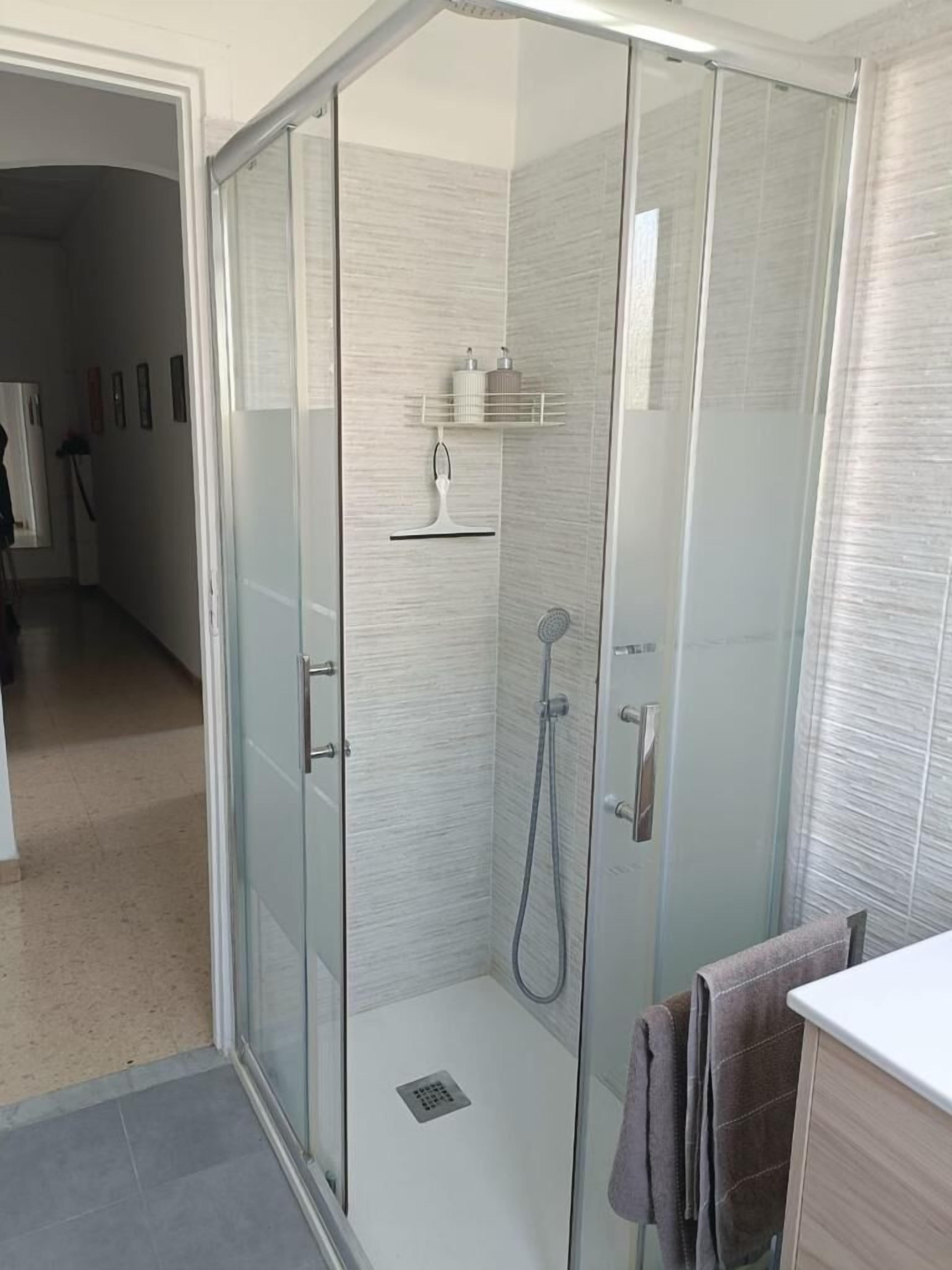 Een moderne badkamer met een douchecabine van glas, een handdoekhouder en een klein plankje met toiletartikelen.