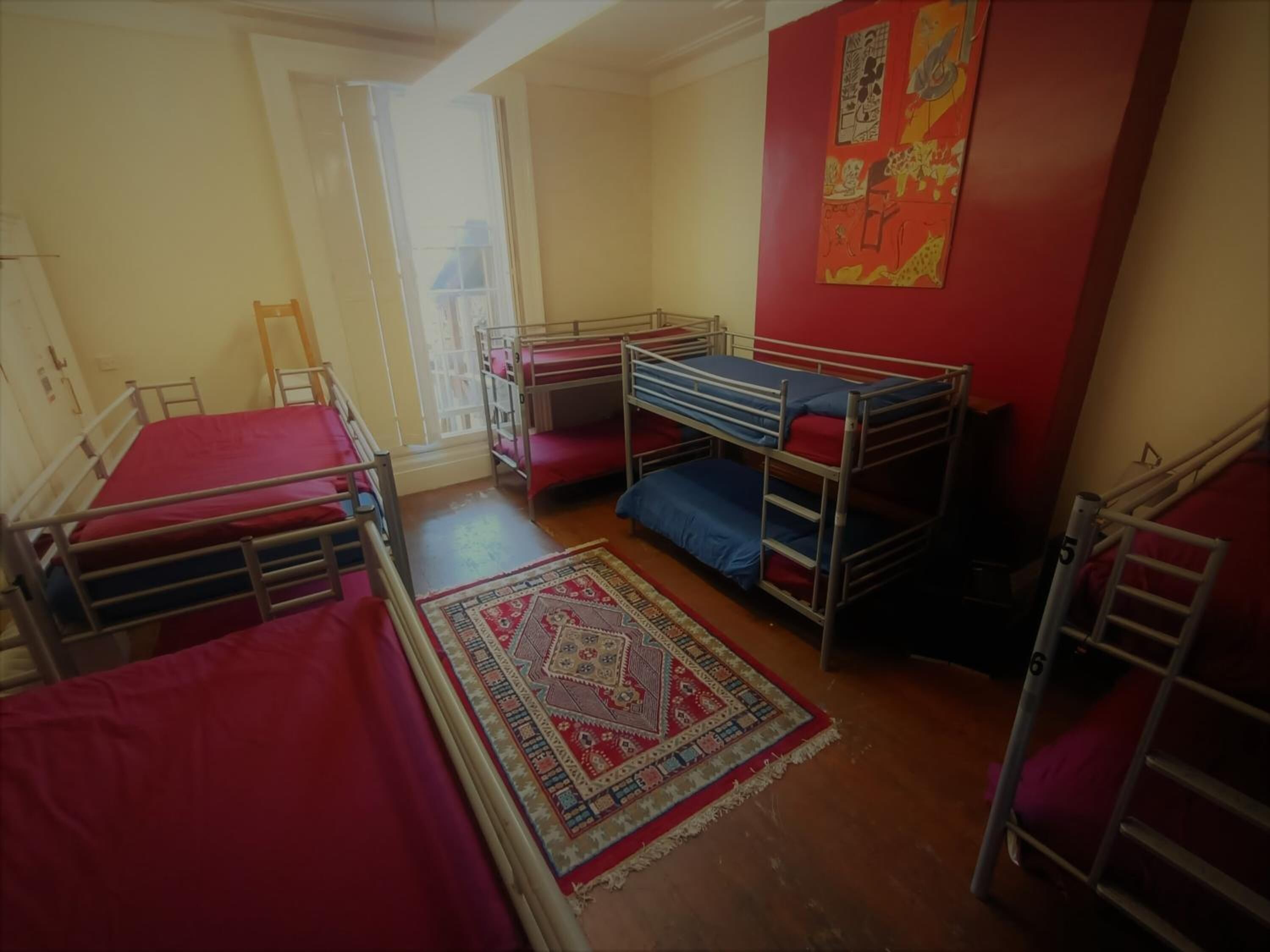 Quarto de dormitório com beliches, tapete estampado e parede vermelha com obras de arte.