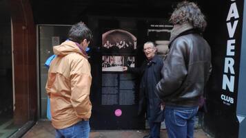 Un grupo de personas de pie frente a una puerta negra con un letrero que dice 'CAVERN CLUB'.