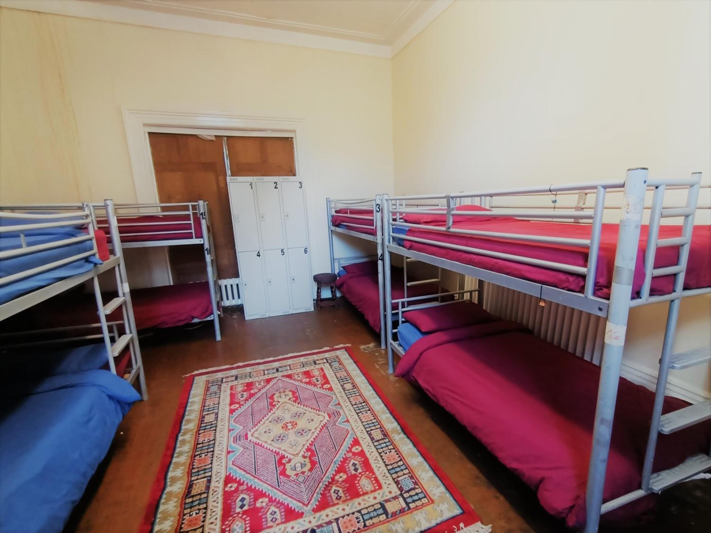 Une chambre de dortoir avec des lits superposés, un tapis à motifs et une porte avec des casiers.