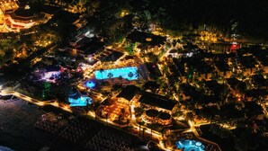 An aerial view of a resort with multiple swimming pools, a beachfront area, and well-lit pathways. - Pirates Beach Club - All Inclusive (Kemer)