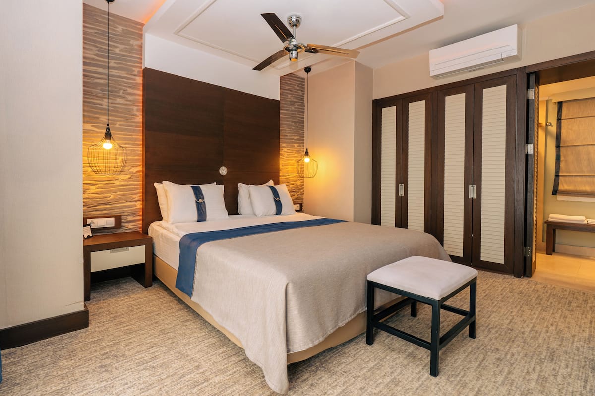 A hotel room with a bed, a bench, a ceiling fan, and a wardrobe.