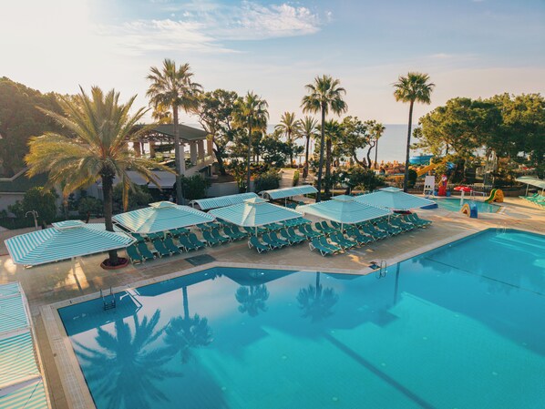 A swimming pool with lounge chairs and umbrellas, surrounded by palm trees and a view of the sea. - Pirates Beach Club - All Inclusive (Kemer)