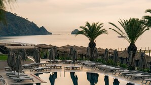 A pool with lounge chairs and umbrellas, a view of the sea, and a mountainous backdrop. - Pirates Beach Club - All Inclusive (Kemer)