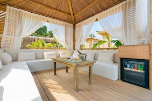 A covered outdoor seating area with a wooden table, white cushions, and a minibar. - Pirates Beach Club - All Inclusive (Kemer)