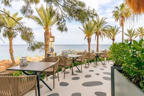 Un'area salotto esterna con tavoli e sedie, una torre dell'orologio e vista sul mare.