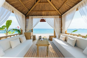 A beachside cabana with a wooden table, white cushioned seating, and a view of the ocean. - Pirates Beach Club - All Inclusive (Kemer)