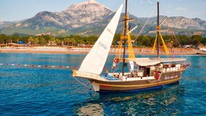A sailboat with a cabin and deck seating, docked near a beach with mountains in the background. - Pirates Beach Club - All Inclusive (Kemer)