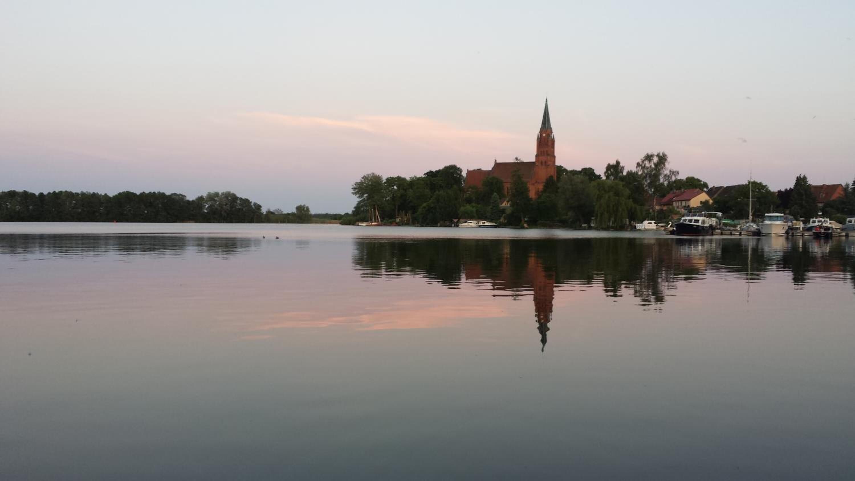 A calm lake with a church and boats in the background.