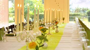 Una larga mesa dispuesta con velas, copas y centros de mesa florales, presumiblemente para un evento formal.